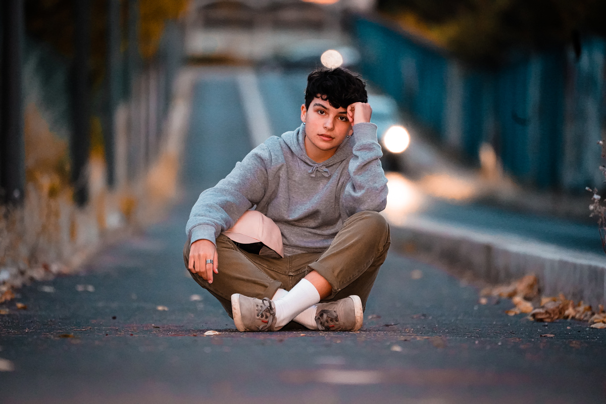 Stylish adolescent resting on asphalt road in evening